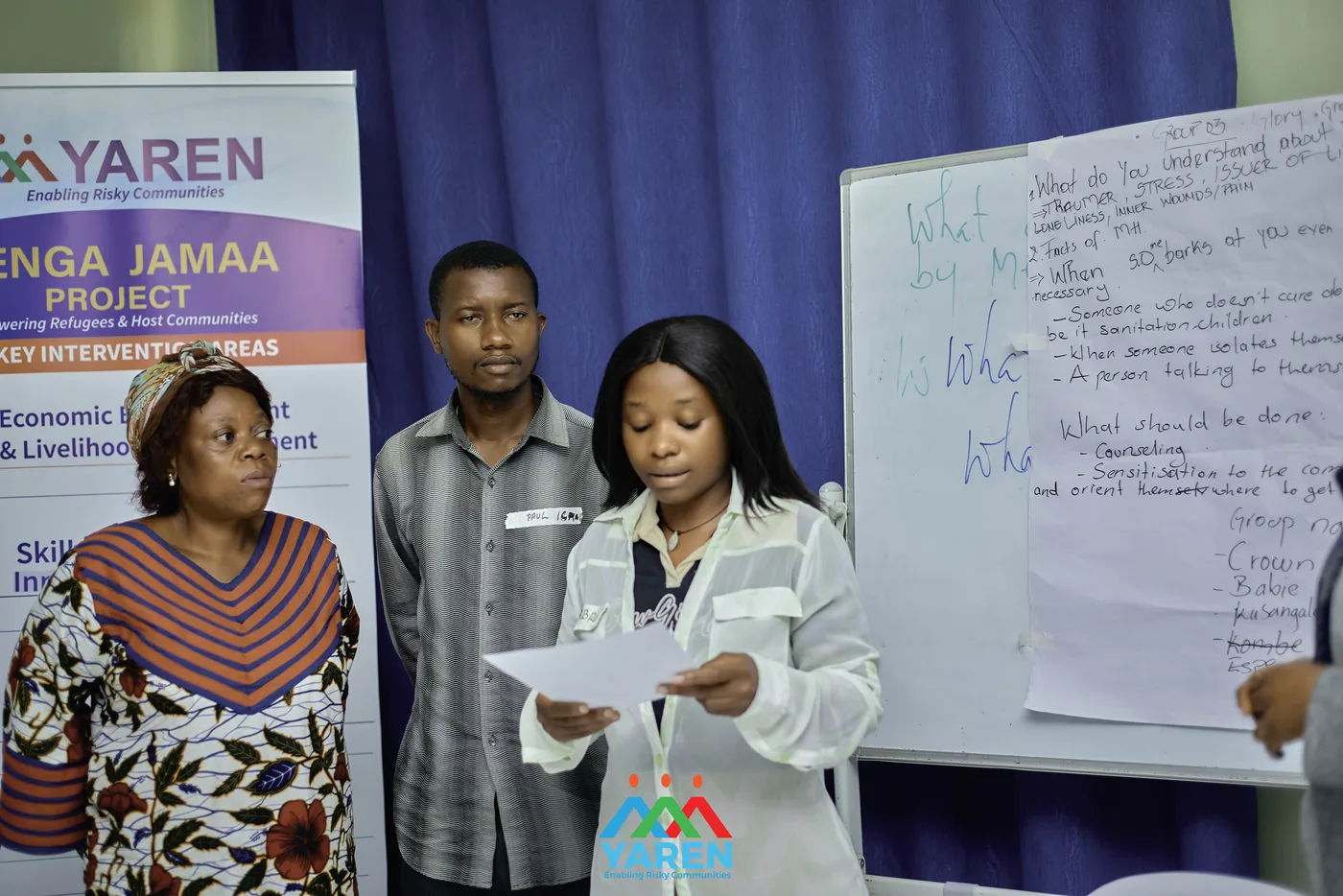 A participant presents a group's findings on a flip chart in front of the Jenga Jamaa banner